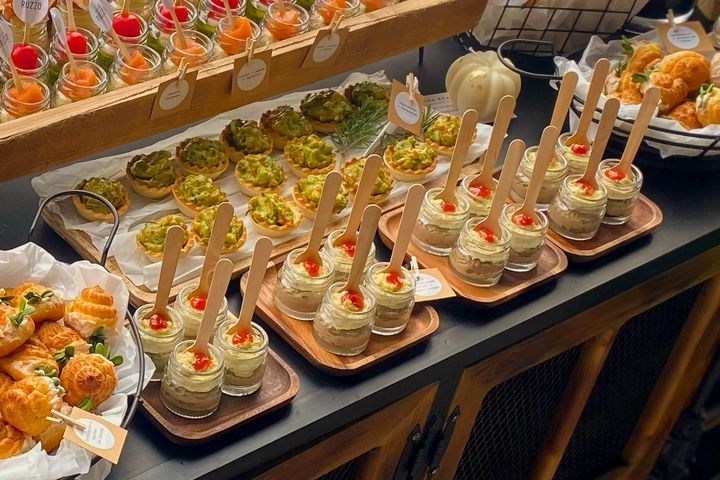 Appetizer cups, avocado tartlets and savory pastries arranged on wooden boards.