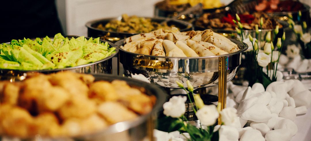 Chafing dishes with crêpes, salad and warm dishes, set among white flowers.