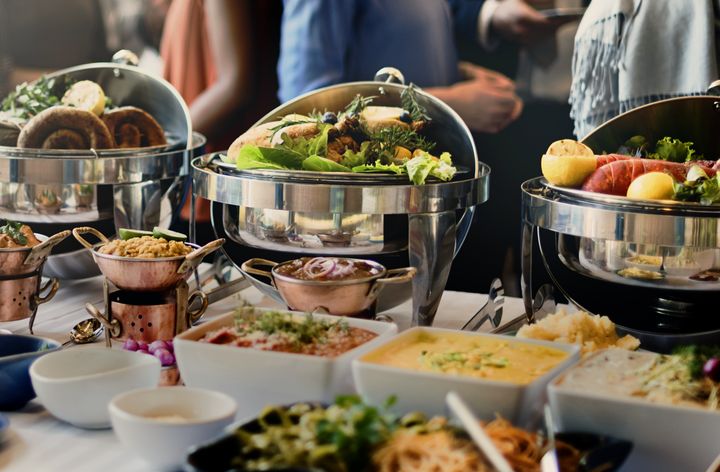 Guests serving themselves at a buffet of chafing dishes with salads, mains and sides.