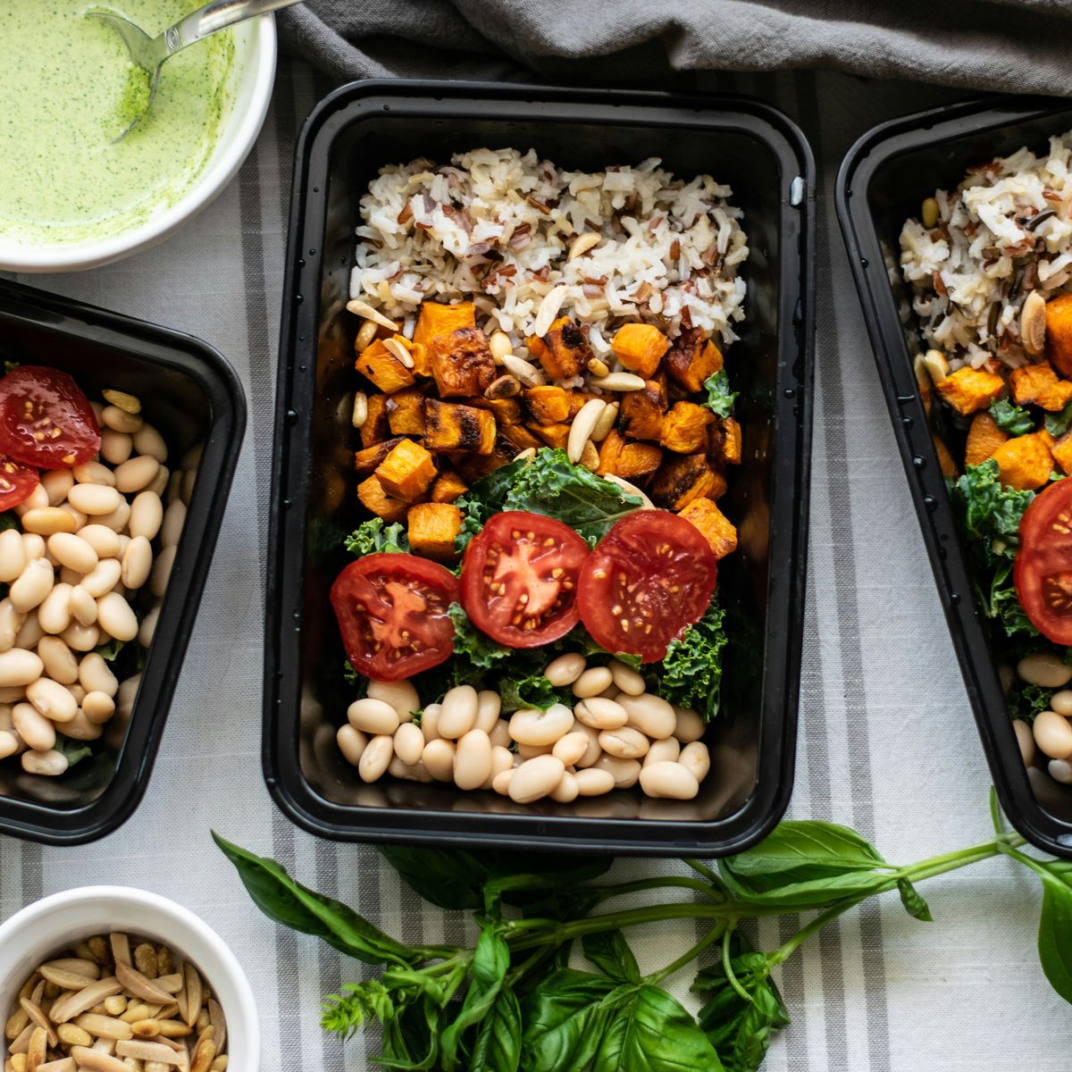 Meal-prep containers with wild rice, roasted sweet potato, kale, tomato and white beans.