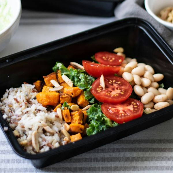 Close view of a container with rice, roasted sweet potato, tomato slices and white beans.