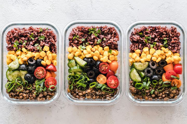Glass containers layered with red rice, corn, olives, tomatoes, cucumber and lentils.
